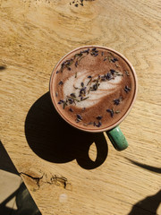 A cool green handmade clue cup of hot cappuccino lavender decorated with latte art on a wooden table in a sunny weather