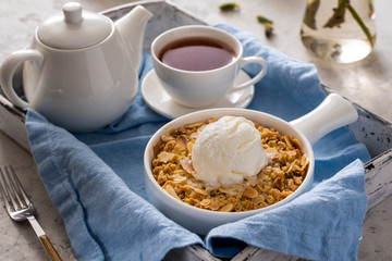 Apple crumble with a scoop of vanilla ice cream and tea on a wooden tray. Breakfast concept