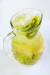 Lemonade of kiwi slices and banana in a tall glass jug on a white background. An isolated object. Vertical photo. Top view.