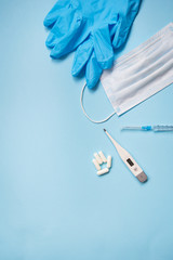 Blue latex gloves on a blue background lie with pills, medical mask, thermometer and syringe