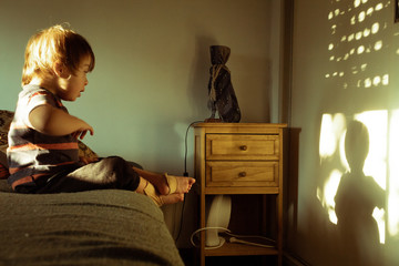 Niño sindrome down juega con su sombra sobre una cama en una tarde de domingo