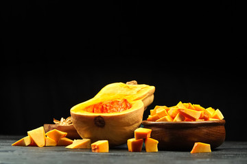 Pumpkin half, fresh pieces in wooden bowl on black background. Chopped raw butternut squash, selective focus