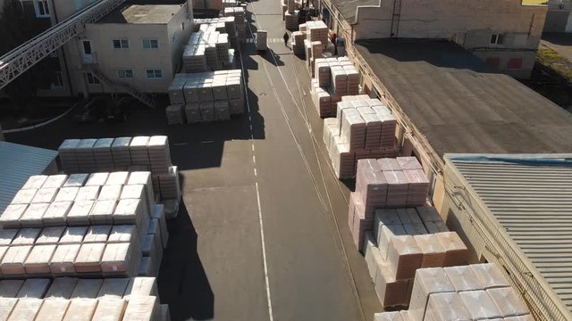 Aerial drone flight over the warehouse. In the storage there are pallets with finished products, cardboard pallets wrapped in plastic film, loaders ride and workers go