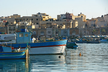 Barcos amarrados en un puerto pesquero de Malta, al fondo se ven las casas del pueblo