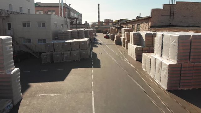Aerial drone flight over the warehouse. In the storage there are pallets with finished products, cardboard pallets wrapped in plastic film, loaders ride and workers go