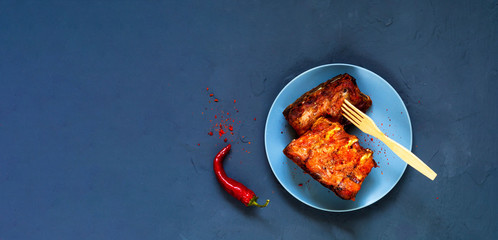 Spicy hot grilled spare ribs from BBQ served with hot chili pepper on blue background. Creative copy space