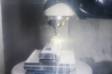 Industrielle moderne CNC Fräsmaschine bearbeitet einen Metallblock aus Edelstahl unter Einfluss von Kühlmittel / Emulsion