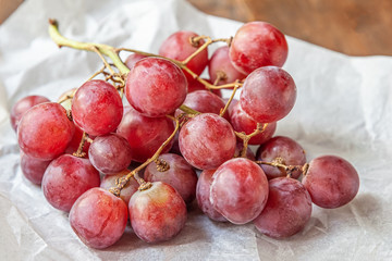 branch of juicy sweet pink grapes on parchment on a wooden table in the kitchen