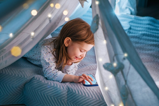 Happy little four years old girl playing in her tent using smartphone