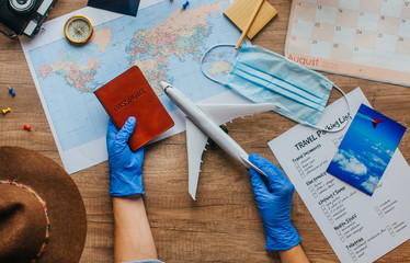 Female hands in disposable gloves holding airplane toy and passport on wooden background