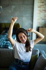 Young cute smiling woman dancing on couch while using wireless headphones at home