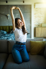 Obraz premium Happy young woman relaxing and stretching on couch thinking of pleasant lazy day