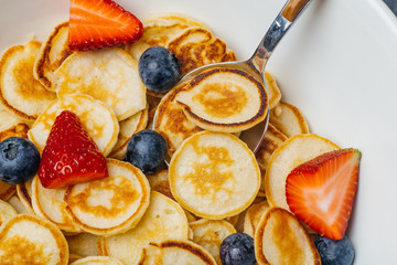 Tiny pancakes for breakfast. Pancakes with strawberries and blueberries cooked in the morning for breakfast in the home kitchen. Food Background.