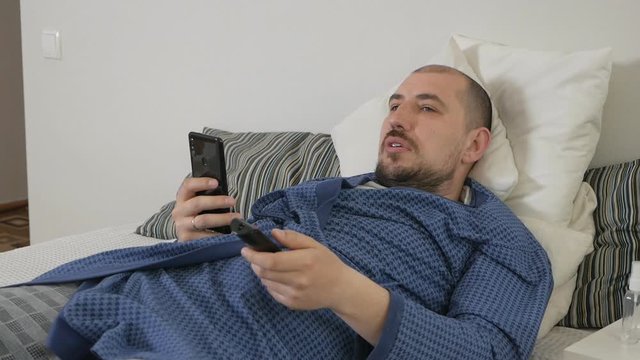 Lazy man using a mobile phone lying on a bed at home