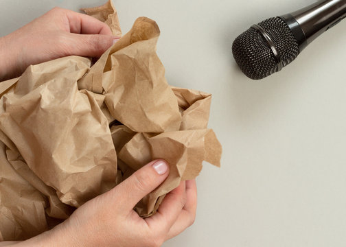 ASMR concept. Specific auditory irritants. Woman's hands crumple kraft paper in front of a microphone. Top view, flat lay.