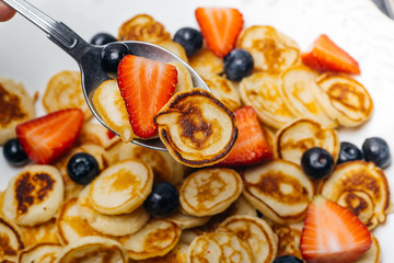 Tiny pancakes for breakfast. Pancakes with strawberries and blueberries cooked in the morning for breakfast in the home kitchen. Food Background.