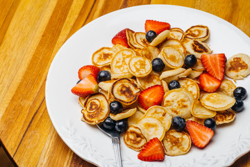 Tiny pancakes for breakfast. Pancakes with strawberries and blueberries cooked in the morning for breakfast in the home kitchen. Food Background.
