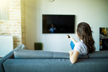 Young woman changing channels with remote control on tv