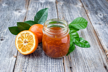 Fresh bitter orange marmalade with ripe fruit offered as closeup on a rustic bleached wooden board...