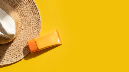 Sun protection objects. Straw woman's hat with sunscreen protection spf cream top view on bright yellow background. Beach accessory. Summer Travel Vacation Concept. Sale kit. Copy space.