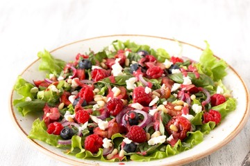 Salad with berries-raspberry, blueberry, sweet cherry, red onion, feta cheese, pine nuts . Dressed with raspberry vinaigrette. Soft focus.