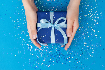Sparkling Gift box wrapped in craft paper and tied with bow in Kid's hands. Concept Father's Day or Birthday greeting card.