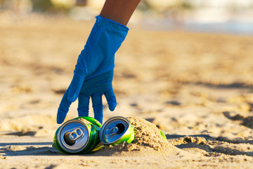 Clean beach from trash. Woman hand picking up empty soft drinks cans trash from the beach