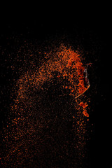 Red paprika spices powder explosion, flying chili pepper isolated on black background. Splash of spice background.