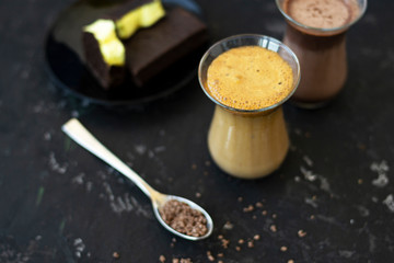 Dalgona coffee and cocoa in glass transparent glasses. Nearby lies a metal spoon with instant coffee, and a chocolate dessert on a saucer