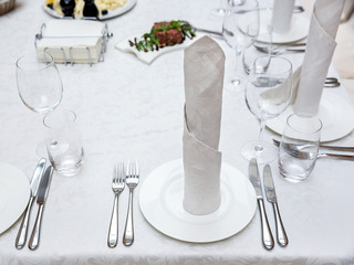 Served banquet table prepared for a conference or a party and covered with a white tablecloth and with a folded cloth napkin on plate