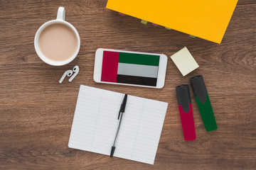 Smartphone with flag uae, wireless headphones, a textbook and a notebook on the desktop, education concept 