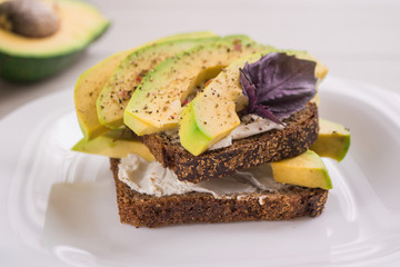 Healthy avocado toasts with rye bread, cream cheese, sliced avocado, basil, salt and pepper ready for breakfast. Vegetarian sandwiches. Clean eating.