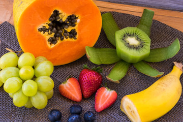 Mix of seasonal fresh fruit on wooden rustic table. Healthy eating with papaya, kiwi, banana, strawberry, blueberry and white grapes