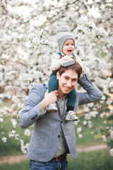 Happy little baby boy and his dad in a blooming Apple orchard
