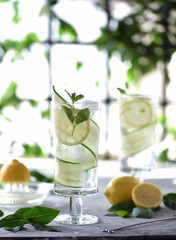 Lime, cucumber, parsley cocktail, lemonade, detox water with ice cubes in a glasses on a white plate. Detox cucumber and mint diet drink, healthy summer cooler.
