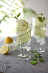 Lime, cucumber, parsley cocktail, lemonade, detox water with ice cubes in a glasses on a white plate. Detox cucumber and mint diet drink, healthy summer cooler.

