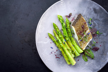 Fried gourmet skrei cod fish filet with green asparagus and lettuce offered as top view on a modern...
