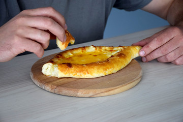 Man eat Georgian bun with hands on wooden cutting board on wooden table