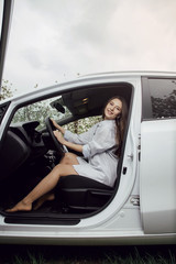 Young woman driving a car. The girl sits in the driver's seat. Young beautiful girl with a nice smile driving a car. View with open car door.