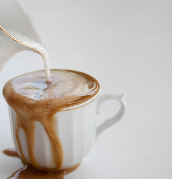 Caf&eacute; con leche en una taza blanca que se derrama sobre la mesa blanca.