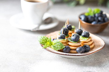 Fashionable food - mini pancakes with blueberries and mint on a light concrete background.