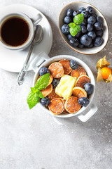 Bowl with tiny pancake cereal on a light concrete background. Trendy food. Mini cereal pancakes with butter, honey and blueberries.
