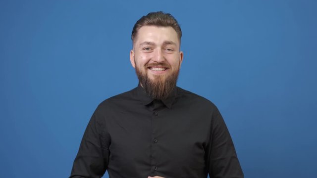 Portrait of a young smiling man with beard on a blue background. Business man in a black shirt
