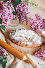 Fototapeta na wymiar Homemade Apple pie on a wooden table next to a bowl of lilacs. Gentle toning.