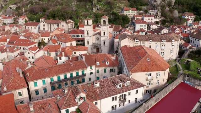 Kotor medieval old town and major tourist destination in Montenegro, featuring The Cathedral of Saint Tryphon from 12th century. Aerial view of vintage stone houses with red roofs, on a sunny day.