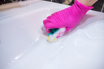 A hand in a pink glove washes a washbasin in the bathroom with a sponge with foaming detergent. Cleaning company cleans the house. Disinfection of the senile node from viruses and bacteria.