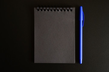 notebook on a spring with black sheets and a blue pen on a black background. space for text