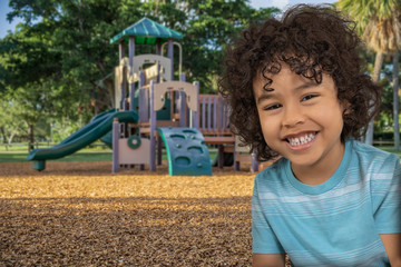 A little boy gets excited to be outside in the playground on a beautiful day. He stops to give a big smile next to his favorite jungle gym slide.