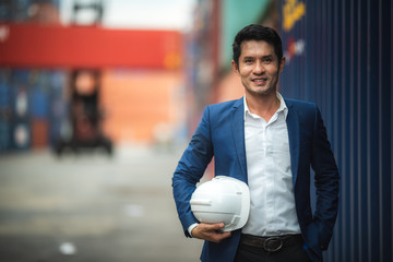 Portrait of a company executive in a warehouse, industrial port area that shows containers for...
