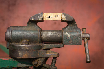 Vice grip tool squeezing a plank with the word croup
